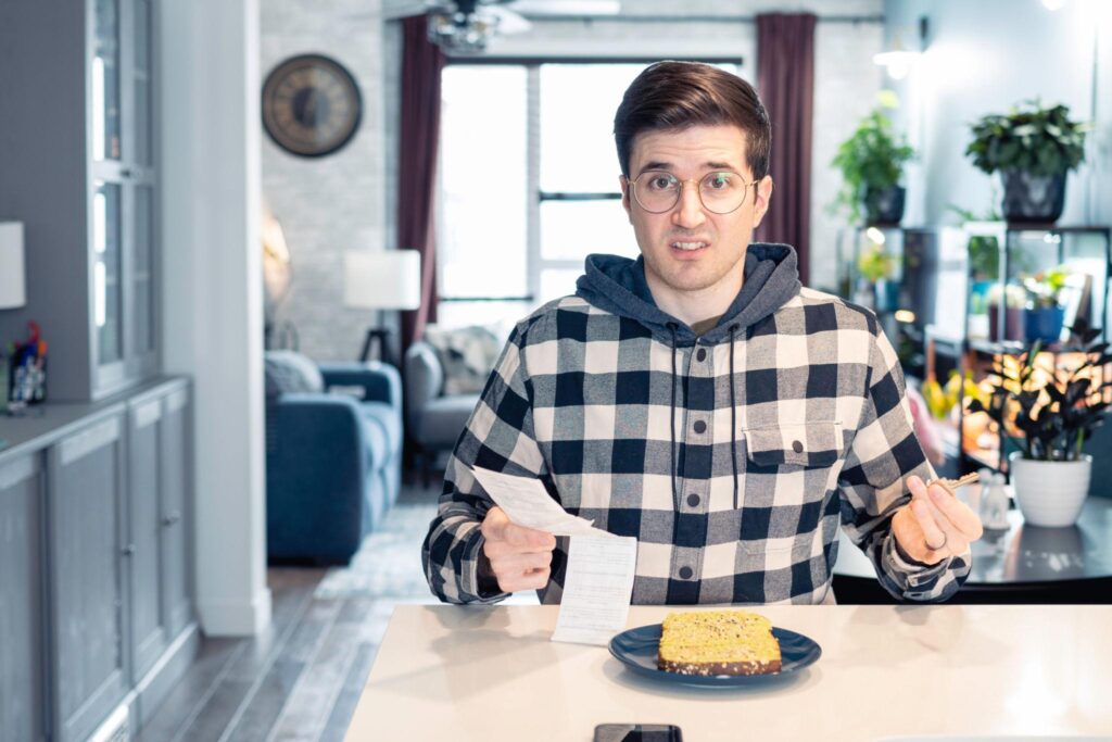 Man looking confused at receipt while sitting at kitchen table with toast.
